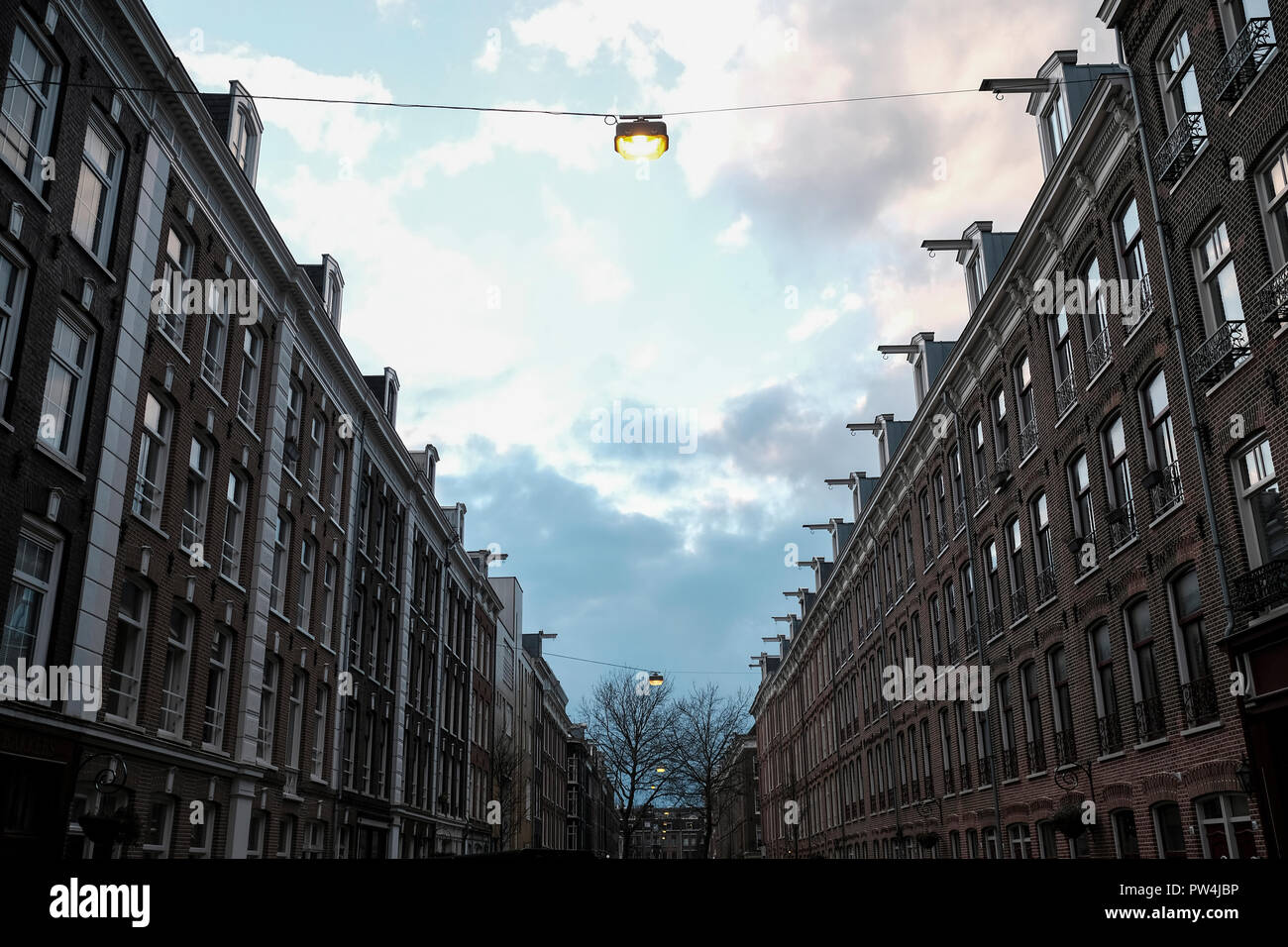 Low Angle Blick auf das beleuchtete elektrische Lampen aufhängen inmitten von Gebäuden gegen bewölkten Himmel in der Stadt Stockfoto