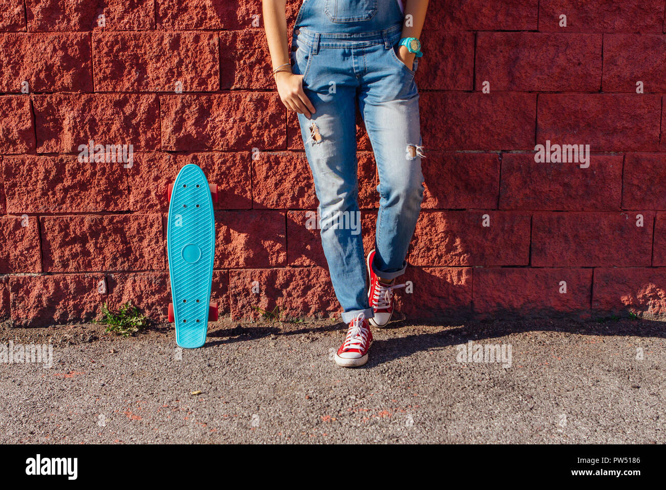 Close up Füße eines Mädchens in rote Turnschuhe und Blue Penny Skate Board mit rosa Räder neben der Wand stehen. Städtische Szene, Leben in der Stadt. Sport, Fitness Stockfoto