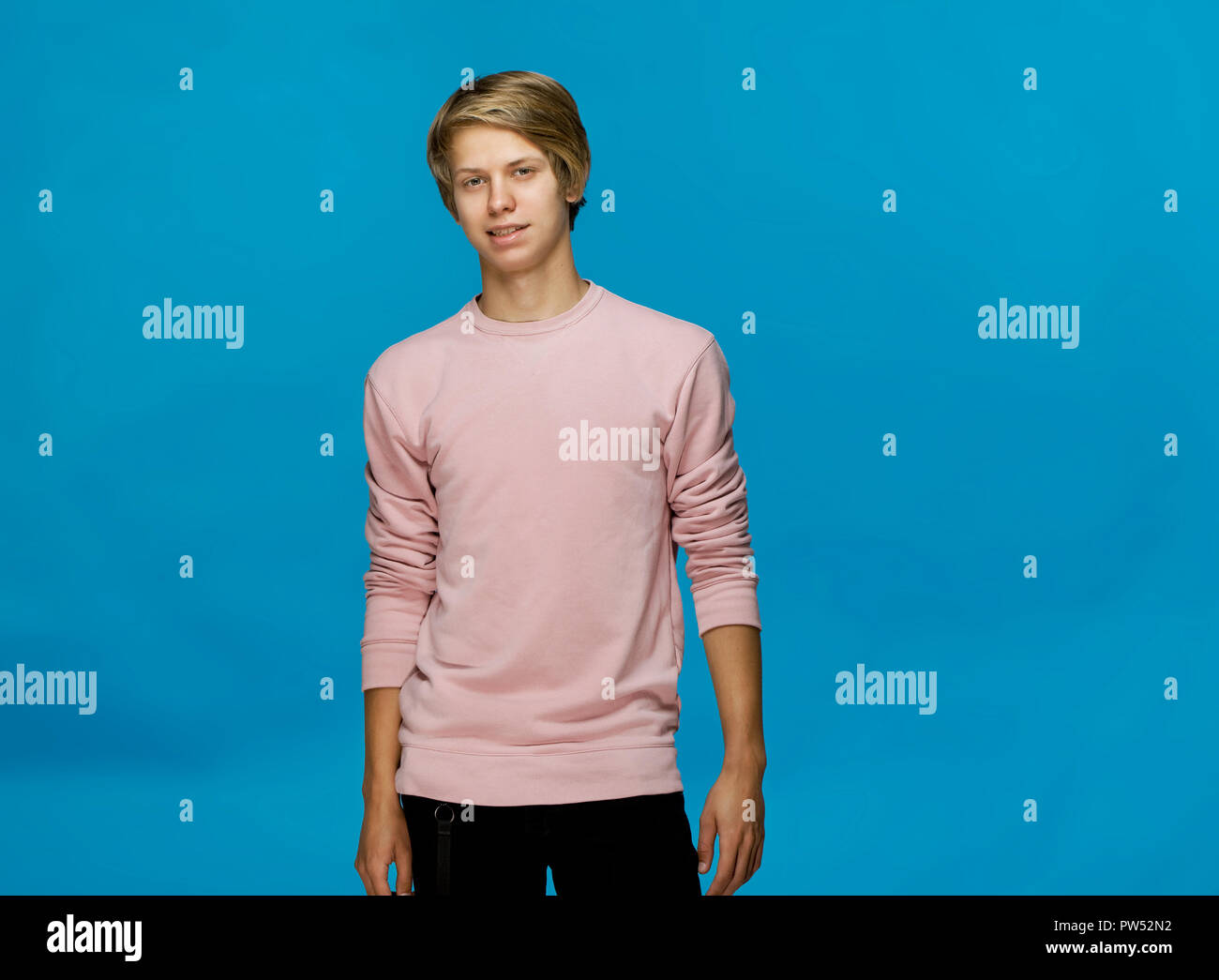 Stattliche glücklich lächelnde junge Mann mit rosa Bluse studio Portrait gegen blaue Wand Stockfoto