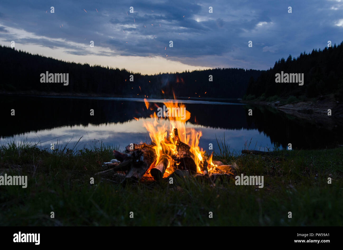 Lagerfeuer nach Sonnenuntergang in den Bergen neben einem See Stockfoto