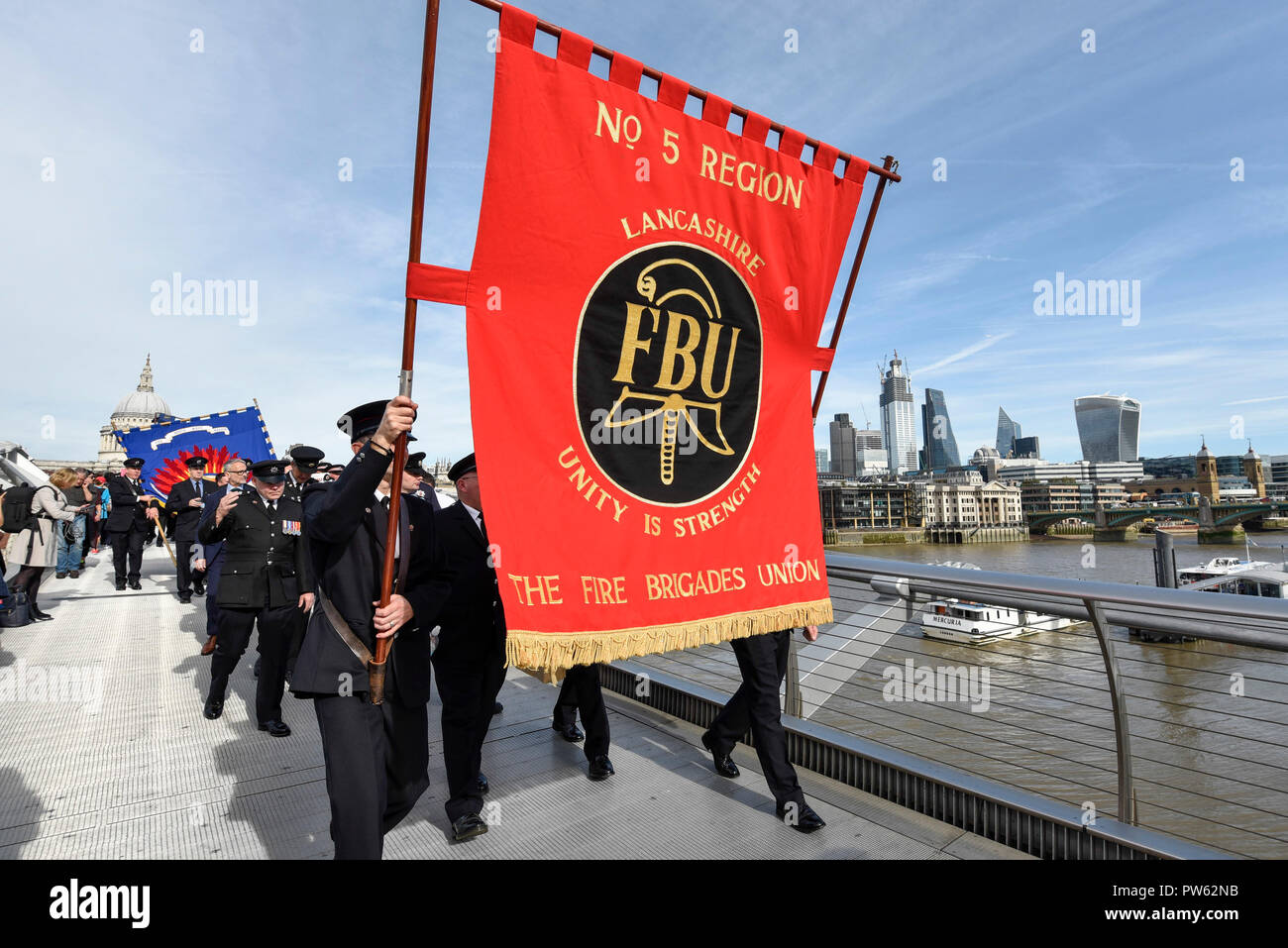 London, Großbritannien. 13. Oktober 2018. Nach einem förmlichen Kranzniederlegung am Nationalen Feuerwehrmänner' Memorial neben der St. Paul's Cathedral, in Erinnerung an gefallene Feuerwehrmänner aus allen Feuerwehr in Großbritannien, Mitglieder der Feuerwehren Union (FBU) Teil in einer formellen Prozession über die Millennium Bridge nehmen, gefolgt von einem Service in Southwark Kathedrale den 100. Jahrestag der Gründung der FBU zu gedenken. Die Aktivitäten sind die bisher größte Festveranstaltung für Feuerwehrmänner, die in der Linie der Aufgabe getötet. Credit: Stephen Chung/Alamy leben Nachrichten Stockfoto