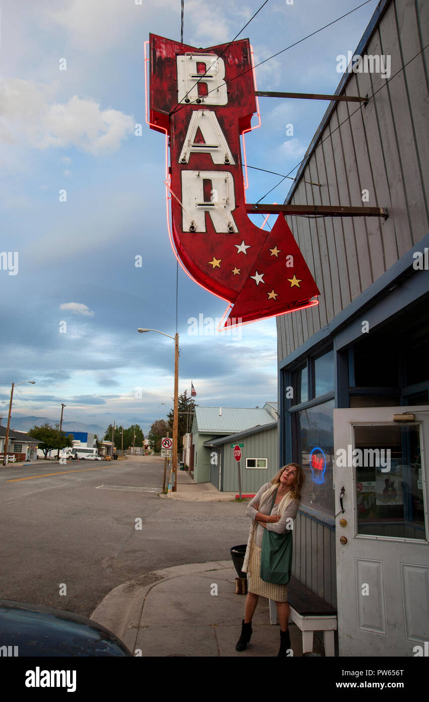 Frau, die ein klassisches Neon-Bar-Schild in einer kleinen Stadt in Montana, USA, anschaut Stockfoto