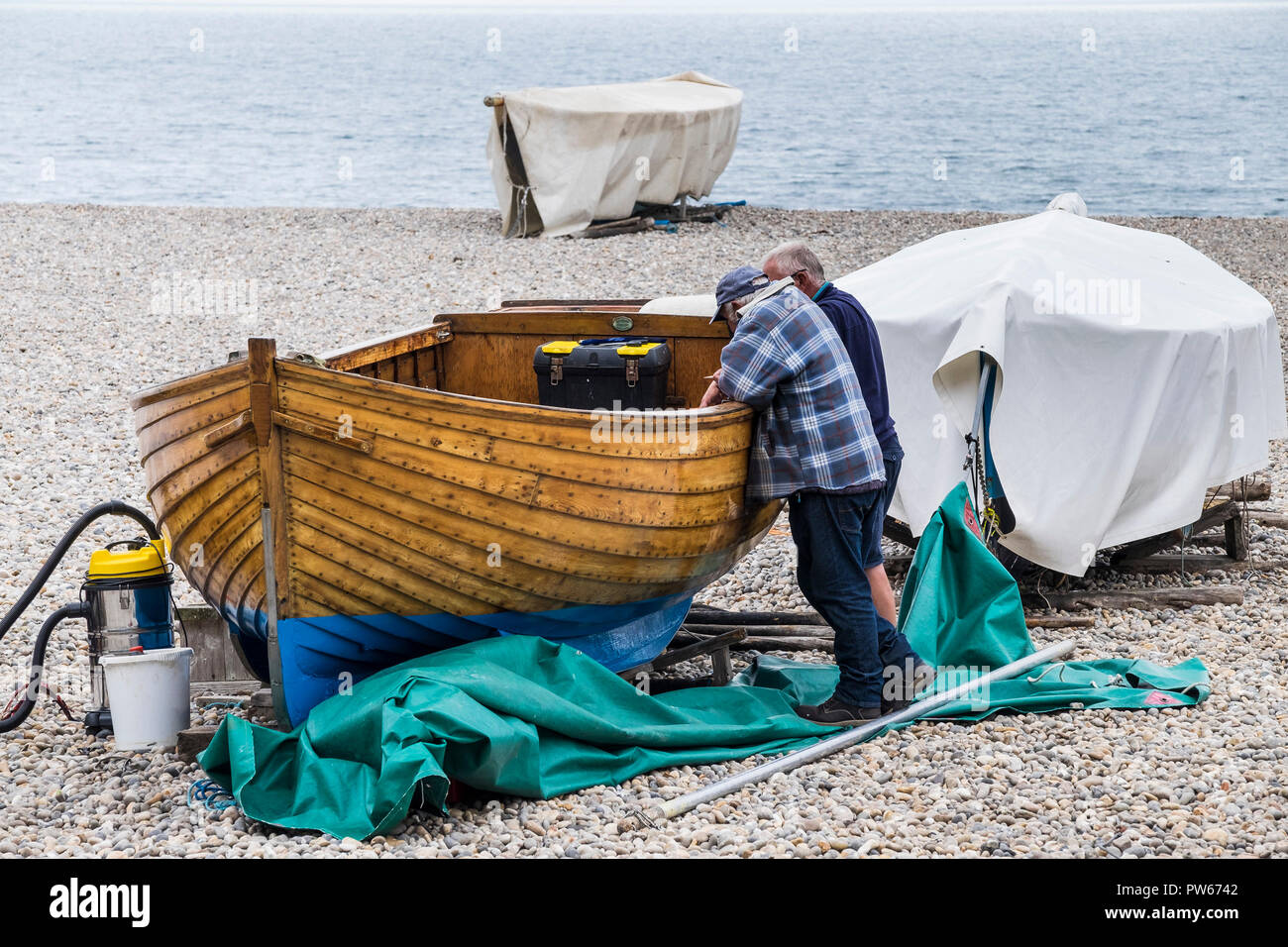 Männer plaudern und lehnte sich auf einem hölzernen Klinker gebauten Boot auf Bier Strand in Devon. Stockfoto