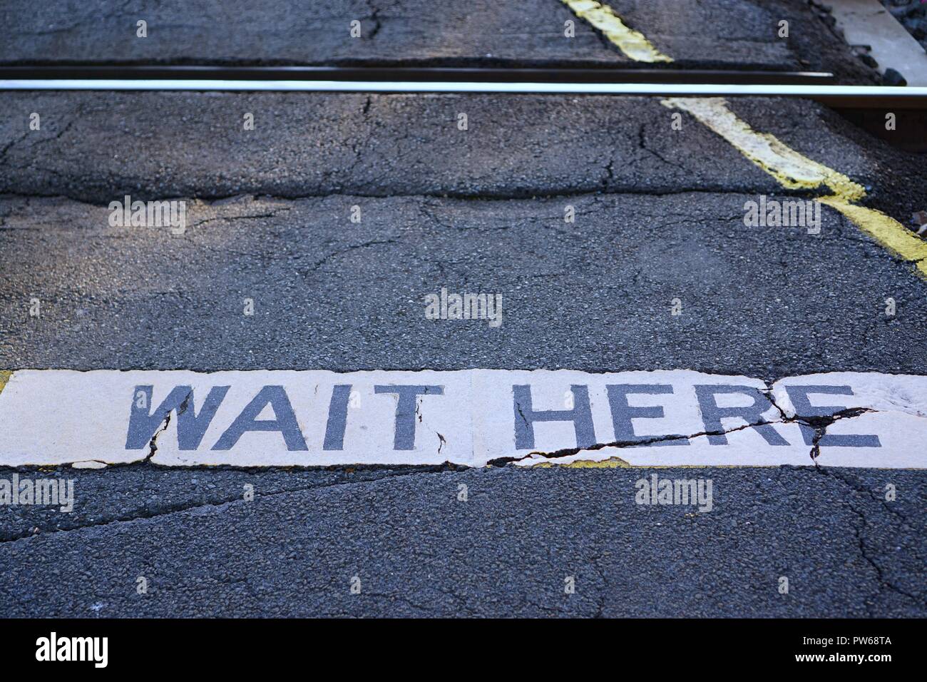 Nahaufnahme der warten hier Schild am Bahnübergang. Stockfoto