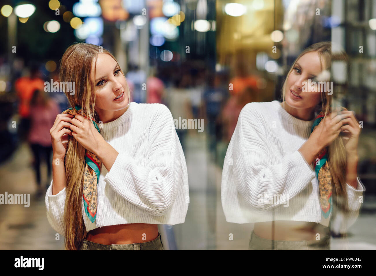 Blonde Mädchen tragen weiße Pullover auf der Straße mit Defokussierten Lichter der Stadt im Hintergrund. Hübsche Frau mit Zopf Frisur bei Nacht re Stockfoto