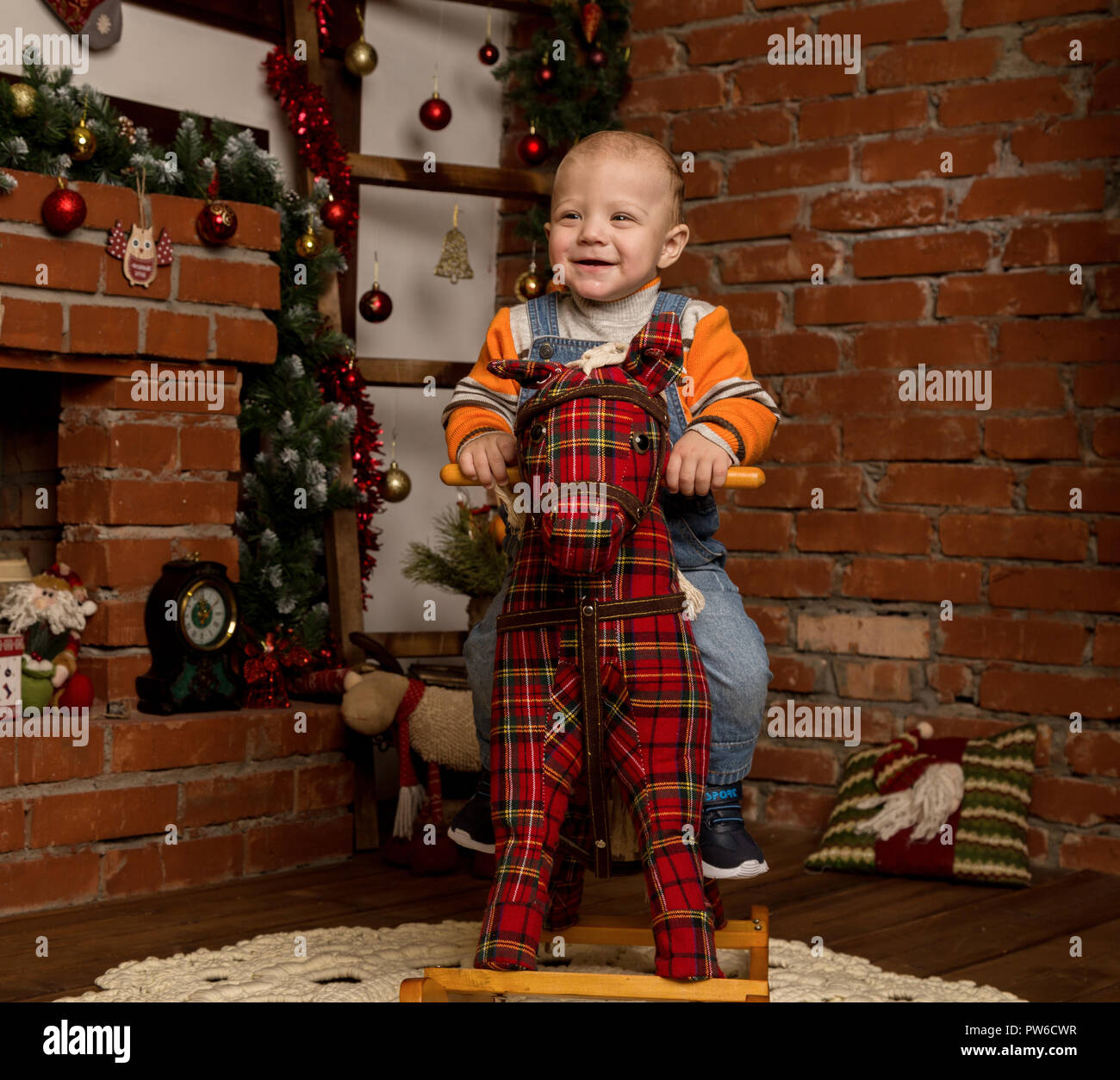Kleines Baby auf Schaukelpferd, in Pullover und Jeans gekleidet. Weihnachten  und neues Jahr Dekorationen Stockfotografie - Alamy