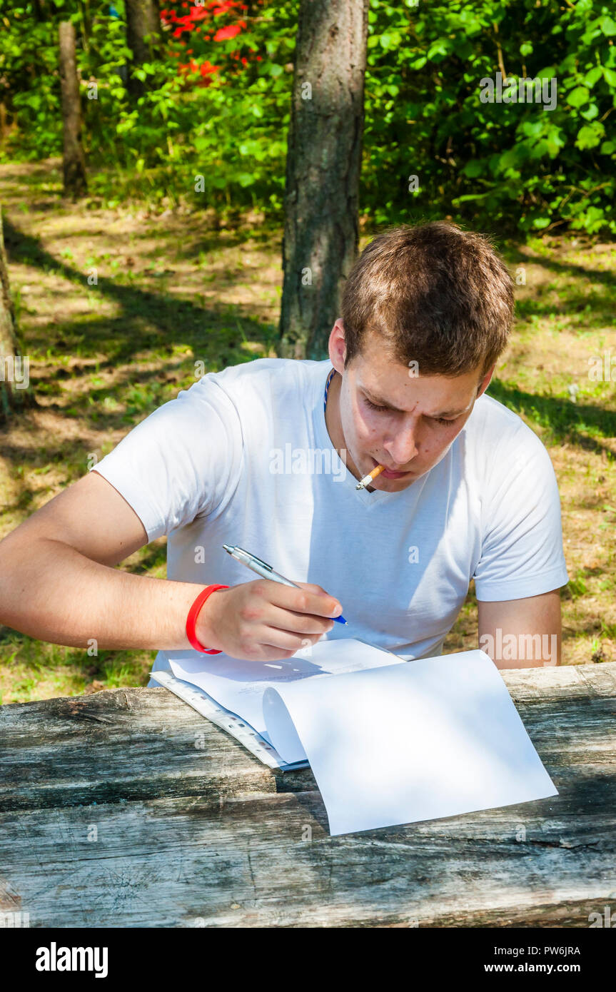 Tiefes denken Kerl, daß das Sitzen auf den ländlichen Holzbank mit Tisch, setzte er seine Ordner von bedruckten Papieren оn der Tabelle, öffnete sie dann auf der rechten Seite, beleuchtete Ein cig Stockfoto