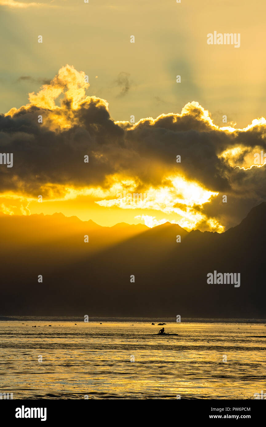 Silhouette von breakig kaykaer, Sonnenstrahlen durch die Wolken über Moorea, Papeete, Tahiti Stockfoto