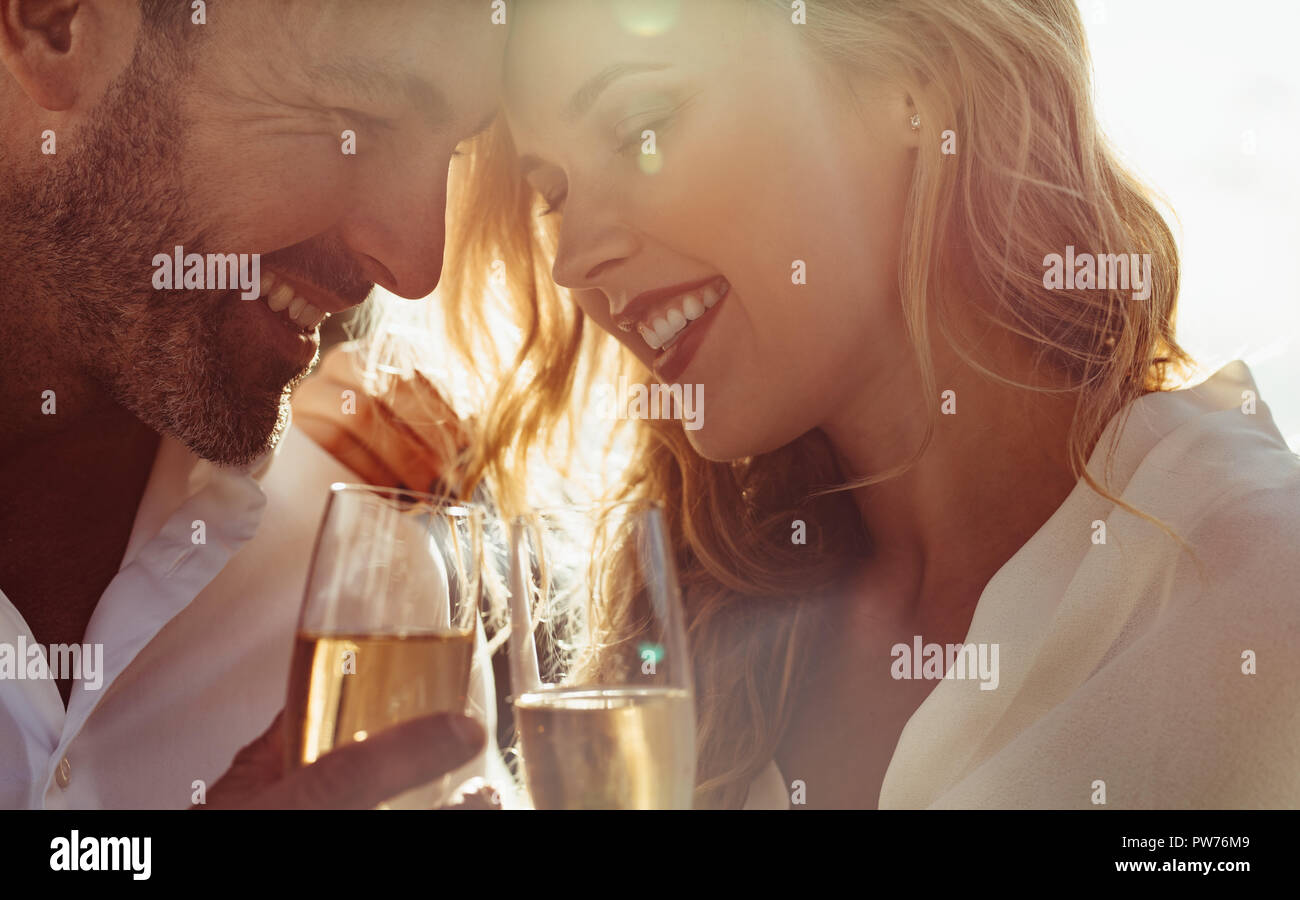 Nahaufnahme von einem jungen Paar mit ihren Köpfen zusammen mit einem Glas Wein und lächelnd. Romantisches Paar mit Wein im Freien. Stockfoto
