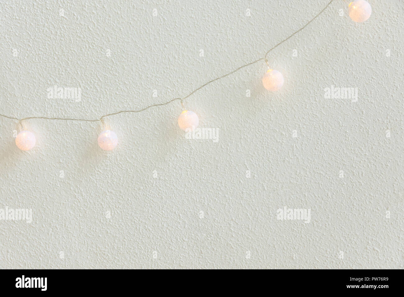 Weihnachten Neujahr Hintergrund. Diagonal hängend Pastell Golden Baumwolle Kugeln Girlande weiße Wand im Hintergrund. Im skandinavischen Stil. Glitzernde Lichter. Gemütliche Stockfoto