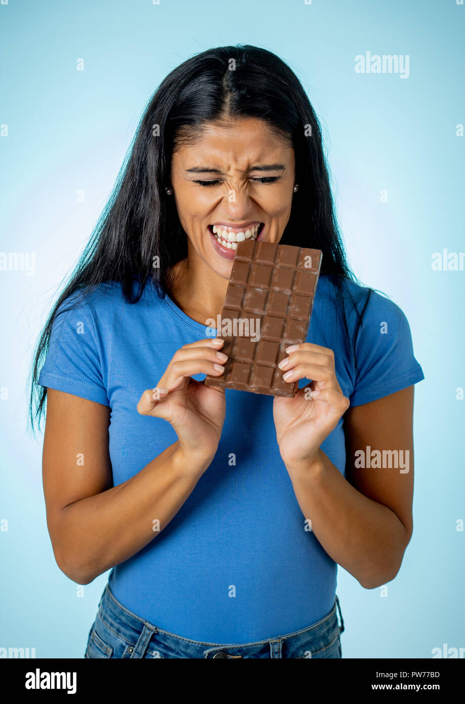 Gerne schöne junge Latin woman holding eine große Tafel Schokolade mit verrückten aufgeregt Gesichtsausdruck in Zucker und ignorieren Diät Konzept Isola Stockfoto