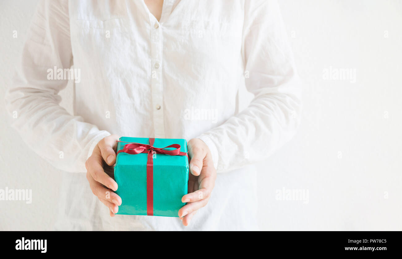 Junge kaukasier Frau hält in den Händen Geschenkbox im Grünbuch mit roter Schleife gebunden. Weißer Hintergrund Pastellfarben. Weihnachten Neue Jahre Valenti Stockfoto