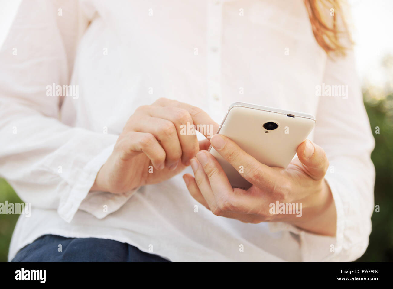 Junge kaukasier Frau sitzt auf der Geländer Geländer hält weiß Smartphone berühren Bildschirm SMS lesen. Moderne Technik natur Kommunikation con Stockfoto