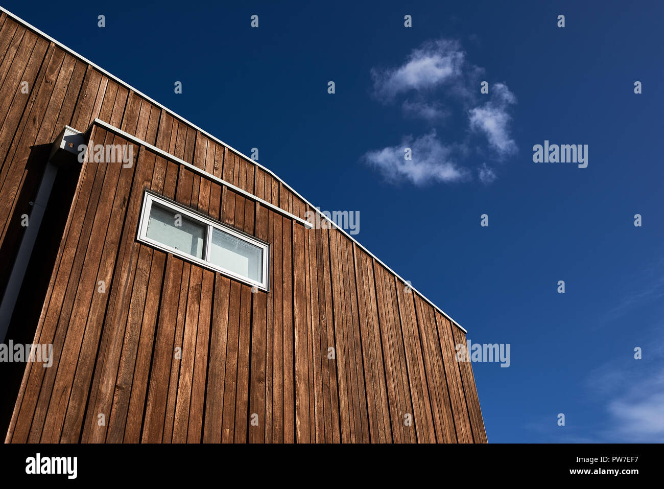 Architektonische Merkmale eines modernen Haus mit Holzverkleidung und einem Fenster gegen einen blauen Himmel mit einer Wolke. Stockfoto