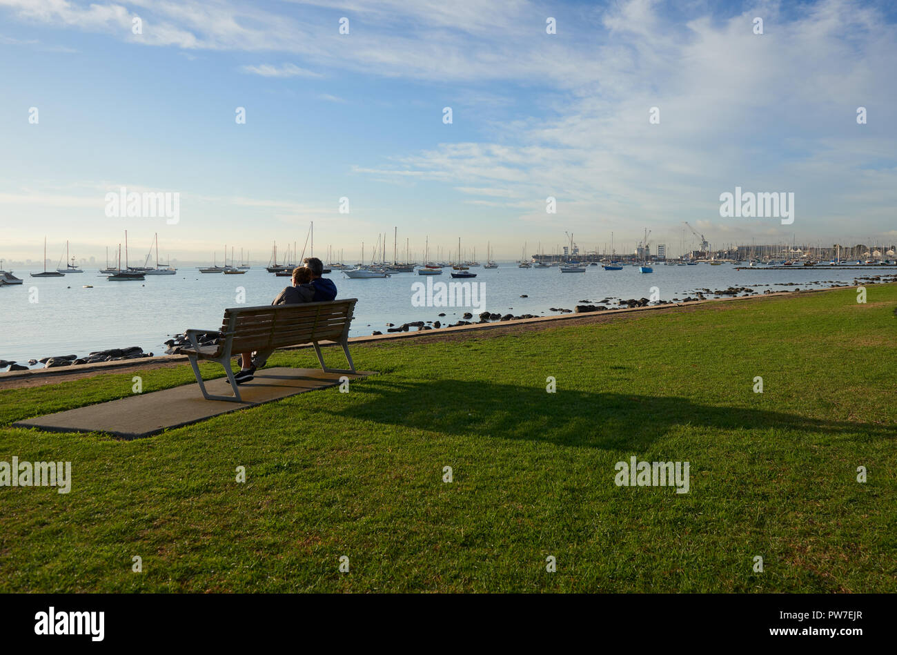 Die Silhouette eines Paar auf einer Bank sitzen durch das Wasser die Sonne genießen und Vista von Wasser und Boote Stockfoto