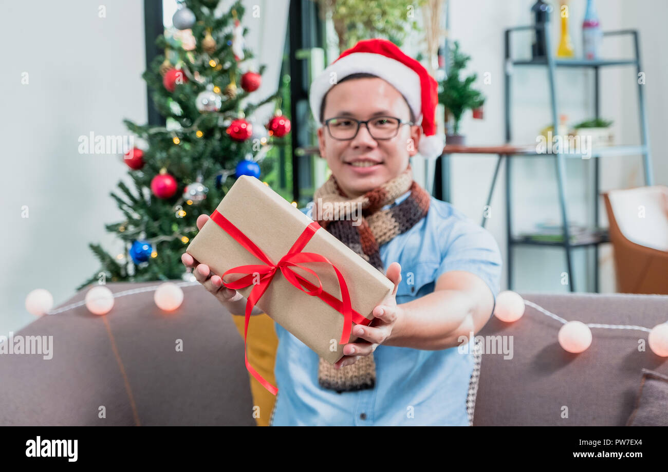 Asiatischer Mann Betrieb vorhanden Box am Sofa sitzen, Geschenk, das im Holiday Celebration Event Konzept Stockfoto