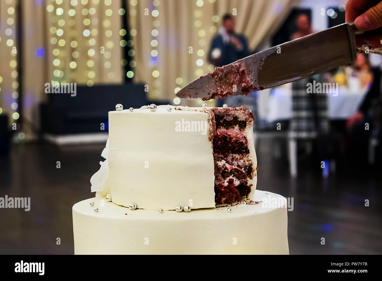 Die erste Stufe einer weißer Dichtmasse Hochzeitstorte in einem Bankettsaal Hintergrund. Hochzeit Kuchen schneiden Sweet Moment. Hochzeit Traditionen. Kuchen art gmbh Stockfoto