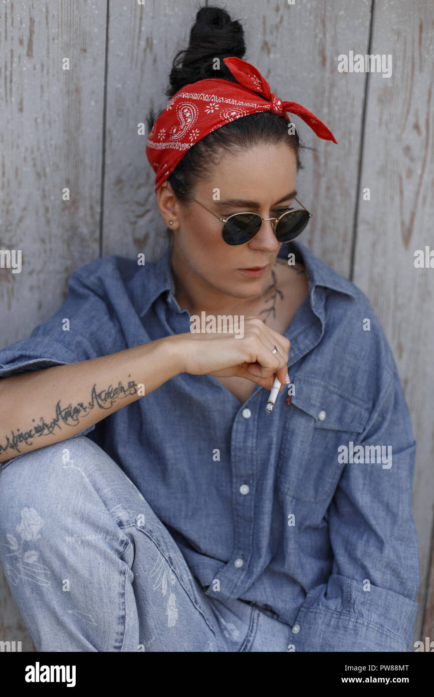 Coole Mode schöne Amerikanische hipster Modell Frau mit Sonnenbrille in  blau denim Vintage stilvolle Kleidung und Jeans in der Nähe von eine  hölzerne Wand saß Stockfotografie - Alamy