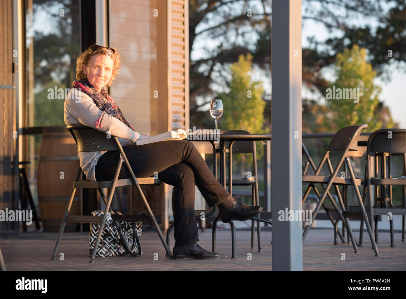 Eine Frau mit einem Buch mit einem Glas Weißwein auf einen Tisch neben ihr in der Nachmittagssonne am Rowlee Weingut in der Nähe von Orange im westlichen New South Wales Stockfoto