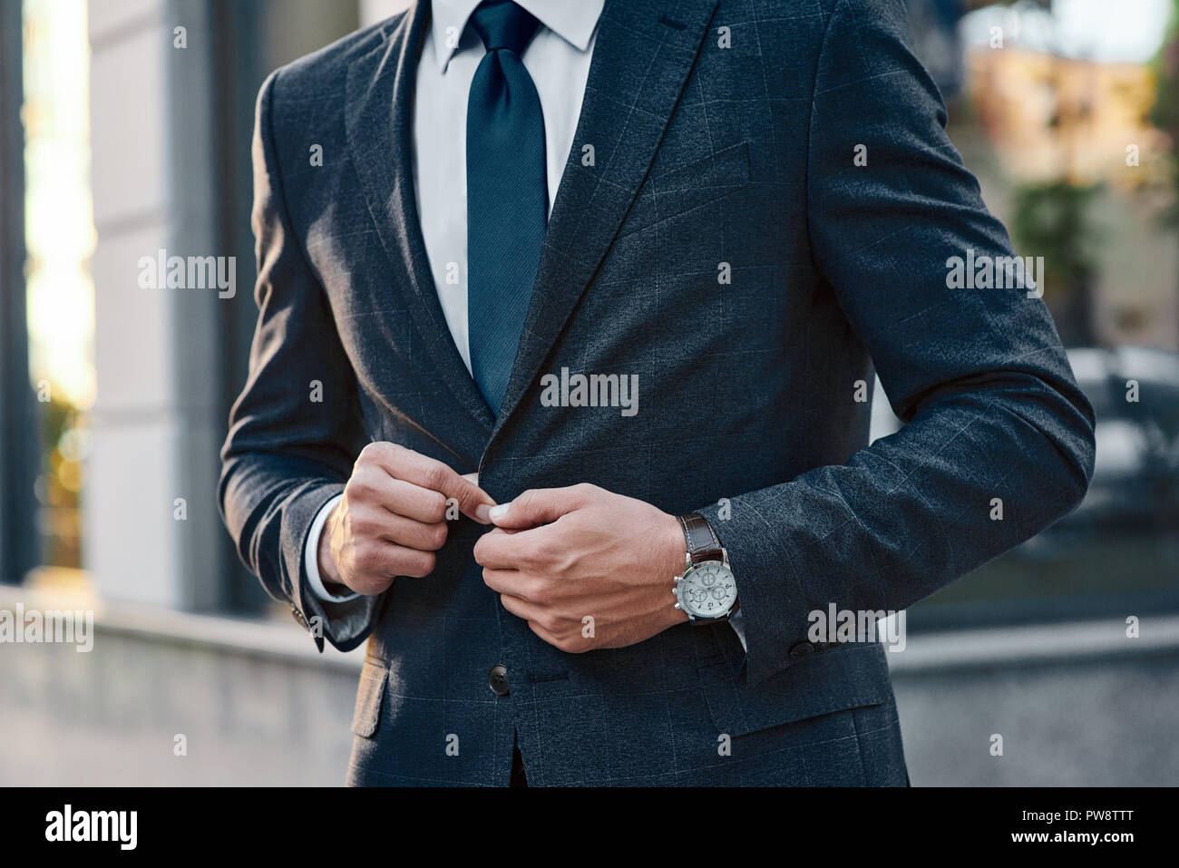 Ein junger Geschäftsmann befestigt einen Anzug Jacke. Er hat auf seinen Händen eine teure beobachten. Stockfoto