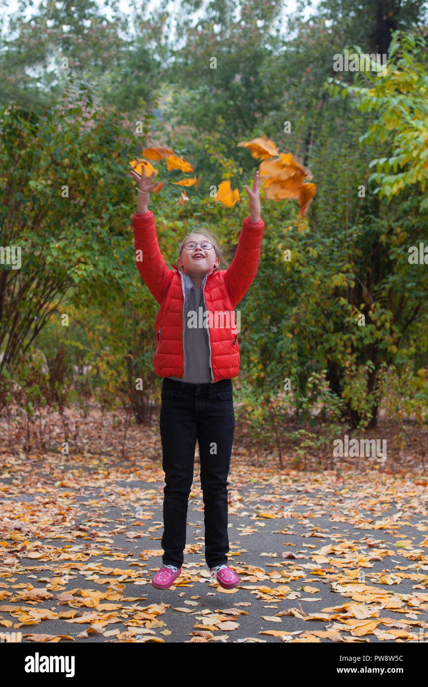 Ein Mädchen mit besonderen Bedürfnissen springen auf einem Hintergrund von Herbst Wald wirft gelbe Blätter Stockfoto