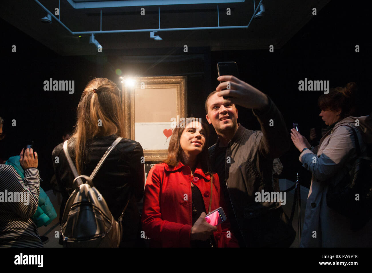 London, Großbritannien. 14. Oktober 2018. Die Besucher nehmen selfies vor banksys "Liebe im bin", die in der Öffentlichkeit bei Sothebys in New Bond Street in London. Die Kunstwerke, die früher als "Das Mädchen mit einem Ballon" bekannt wurde geschreddert Momente nach dem Zuschlag und der Hammer fiel bei Auktion an einen ausländischen Käufer am 5. Oktober Credit: Amer ghazzal/Alamy Live News Credit: Amer ghazzal/Alamy leben Nachrichten Stockfoto