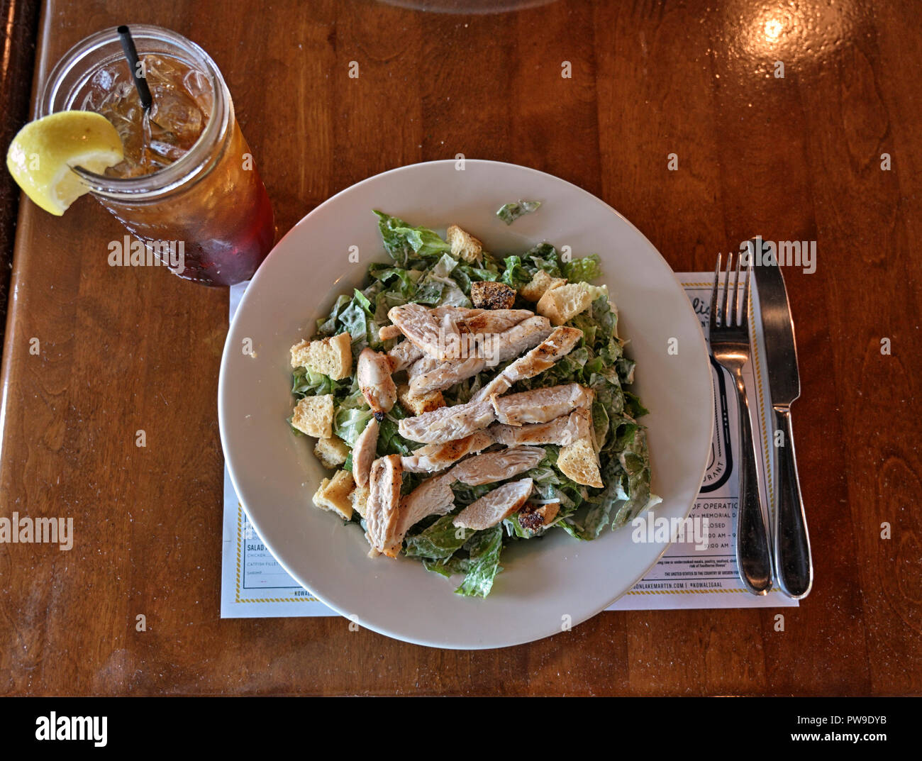Hühnchen Caesar Salat und einem Glas Eistee, von oben, auf einem Tisch im Restaurant. Stockfoto