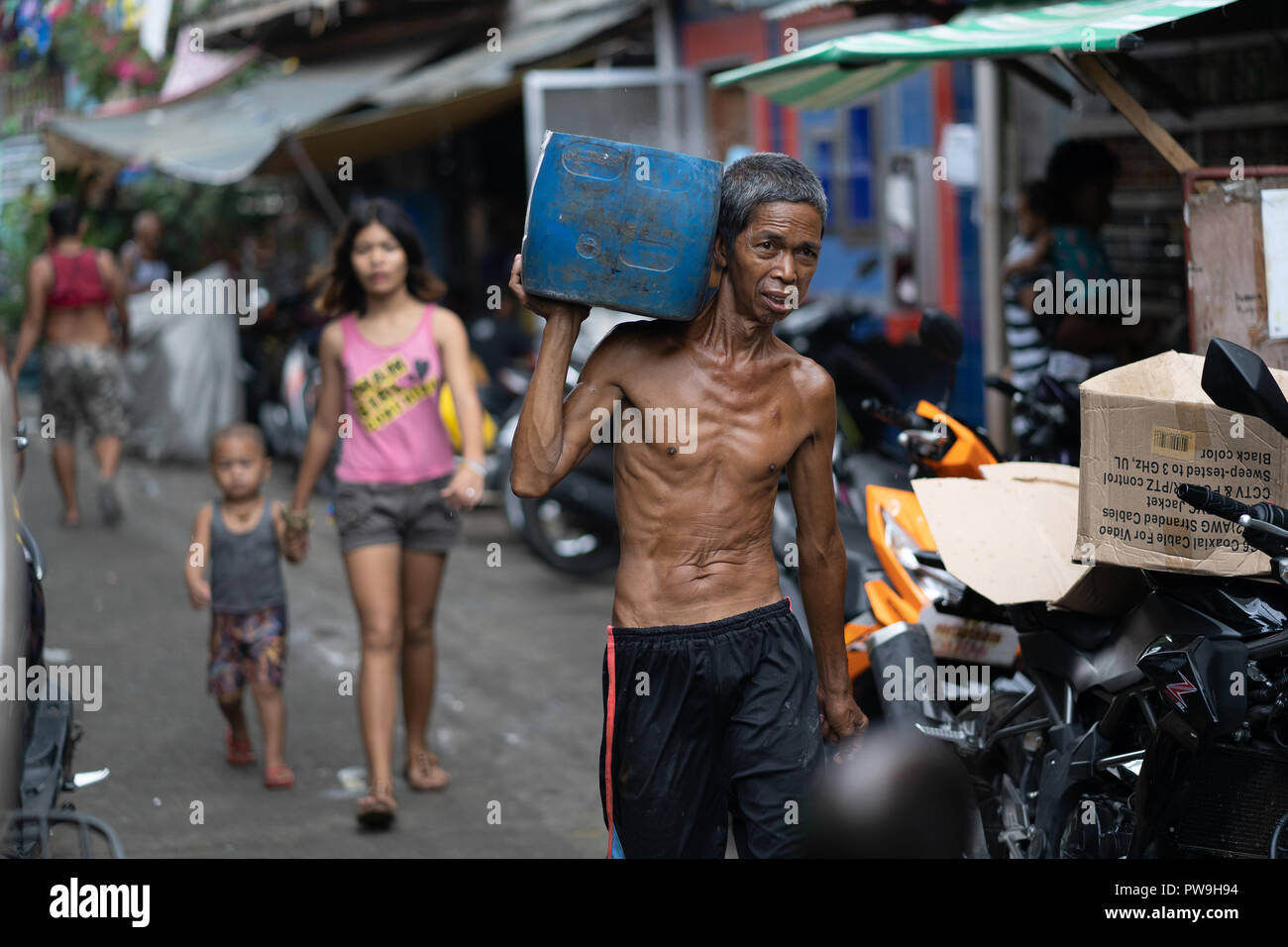 Ein Filipino Mann, der einen Kunststoffbehälter durch ein slumgebiet von Cebu City, Philippinen Stockfoto