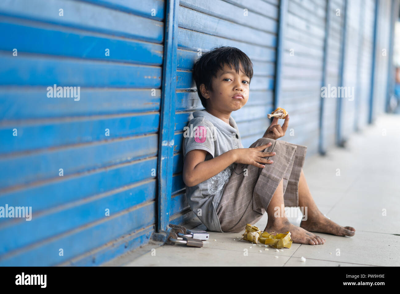 Eine junge philippinische Jungen mit schmutzigen Füße als Folge der keine Schuhe isst eine Mahlzeit auf dem Bürgersteig, Cebu City, Philippinen Stockfoto