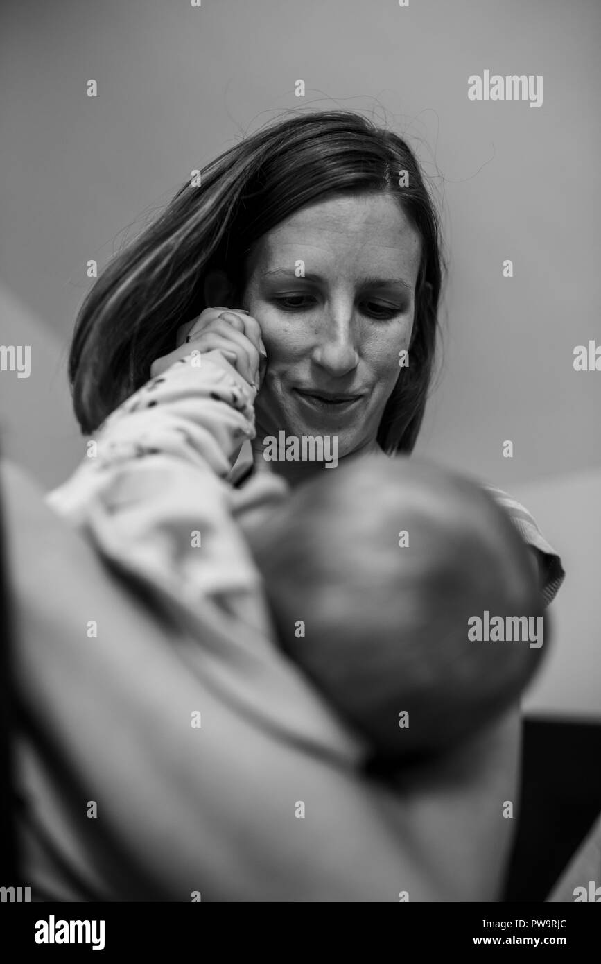 Monochromes Bild der jungen Mutter liebevoll halten Ihr Baby und spielen mit ihren kleinen Hand. Stockfoto