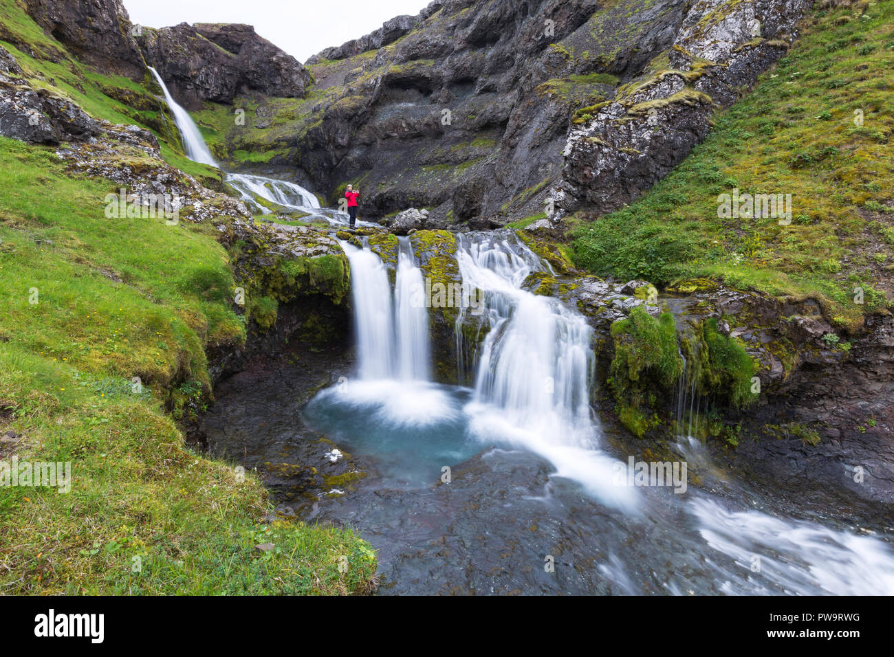Fotograf bei kleinen Wasserfall vor den Toren der Stadt Grundarfjörður auf der Halbinsel Snaefellsnes, Island Stockfoto