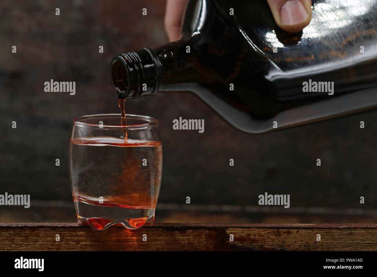 Rum ist aus der Flasche in ein Glas gegossen, auf dunklem Hintergrund serviert. Stockfoto