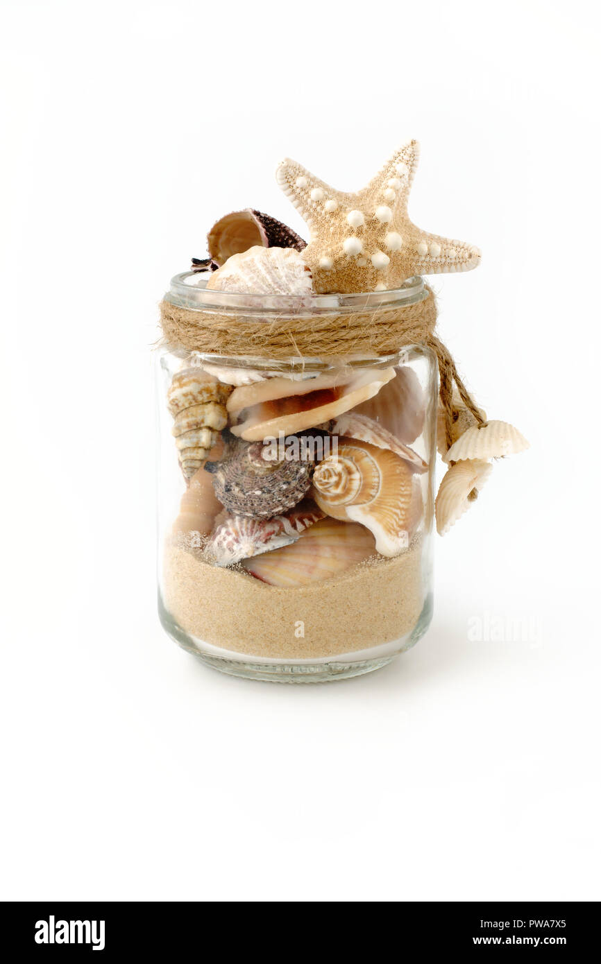 Vielzahl von Muscheln und Sand in einer handgefertigten Glas Glas mit mini Muscheln dekoriert und auf weißem Hintergrund. Low Angle View. Stockfoto