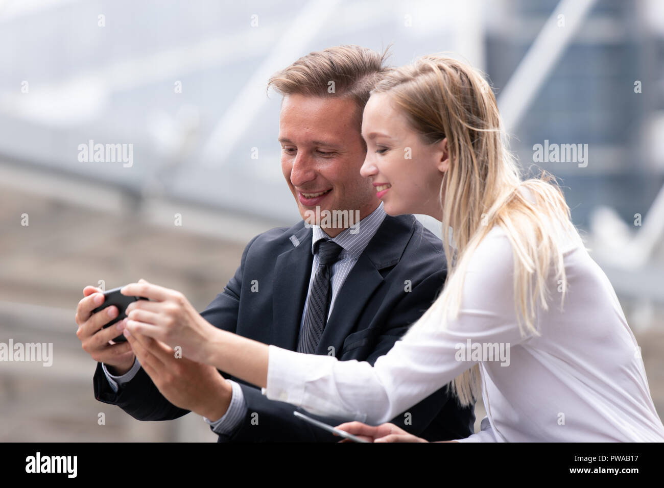 Paar business Leute, die auf der Suche am Smartphone zusammen und Lächeln im Freien Bürogebäude Hintergrund. Stockfoto