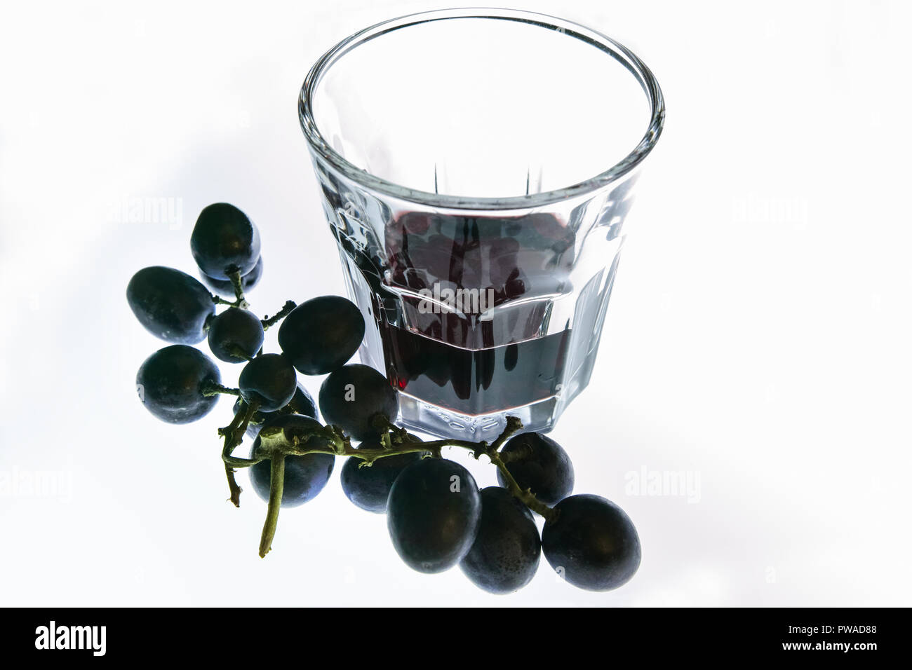 Ein Cluster von blauen Trauben sind neben einem Glas schwarzen Wein gelegt. Beide haben die gleiche Farbe. Stockfoto