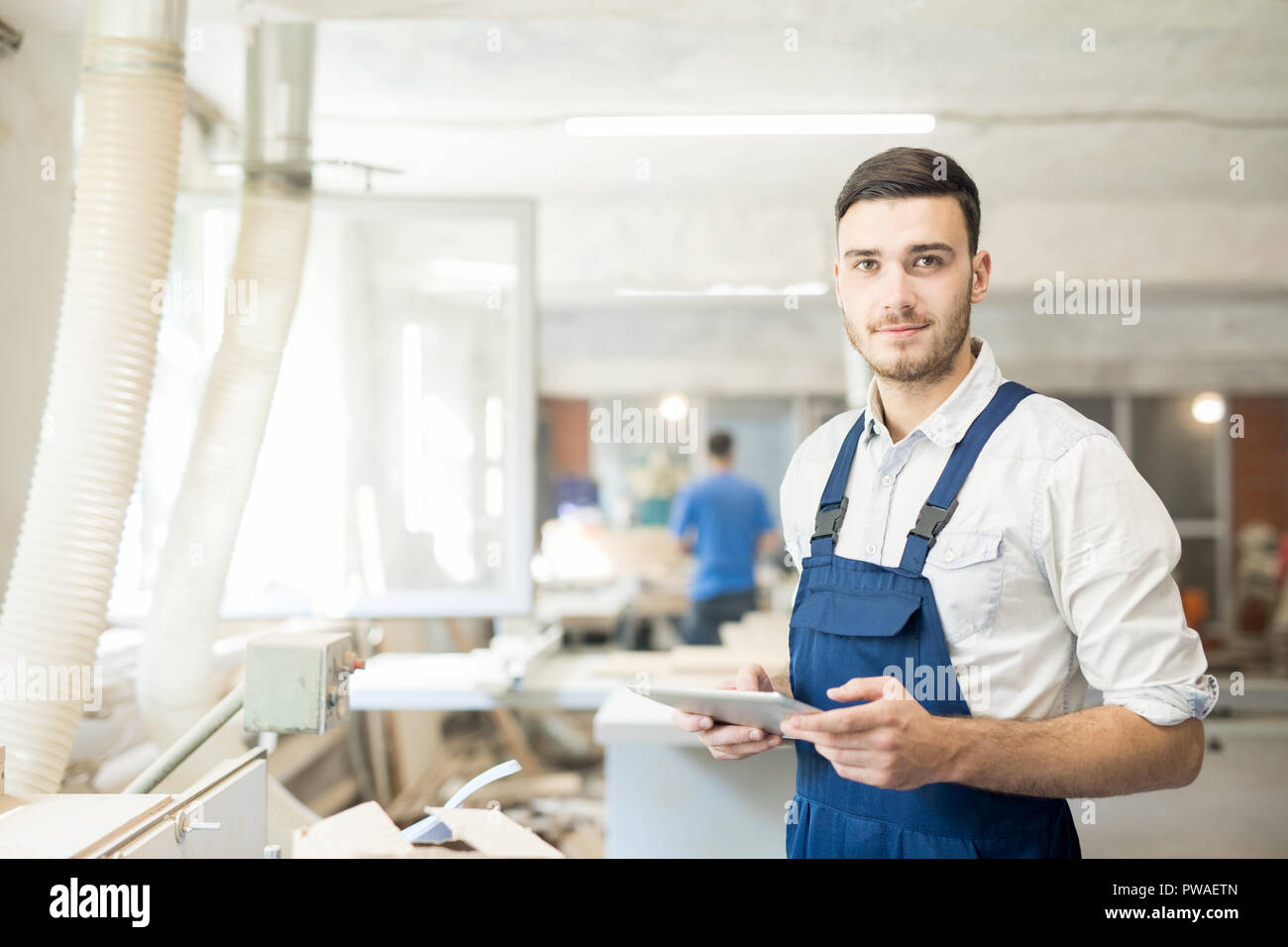 Junge Arbeitnehmer in Latzhosen zu Ihnen schauen während Vernetzung oder Schauen durch online-Daten Stockfoto