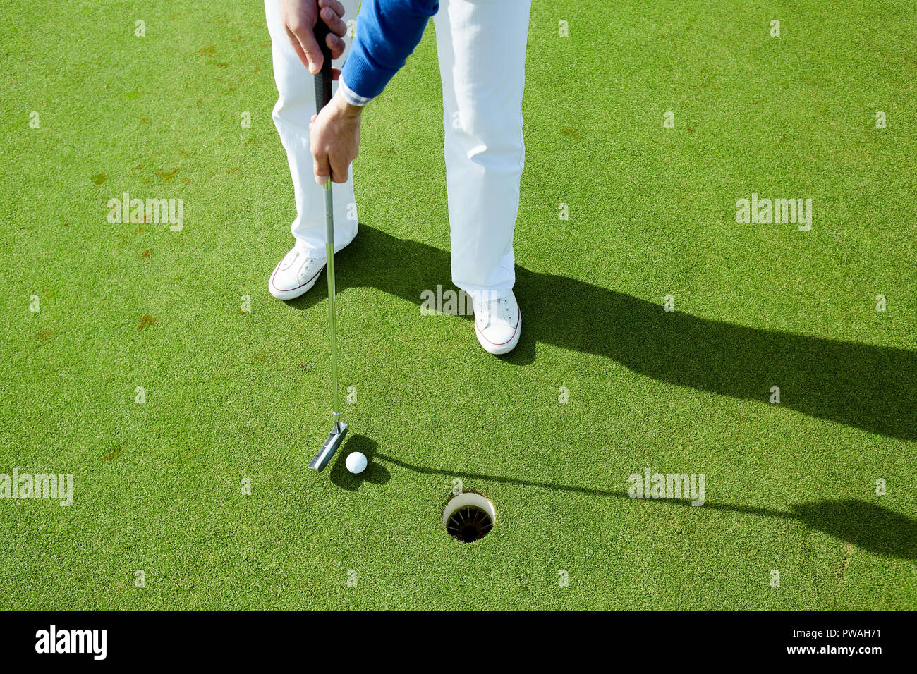 Mann in weißen Hosen und Schuhe stehen auf grünen Rasen und gehen Golf Ball in das Loch zu schlagen Stockfoto