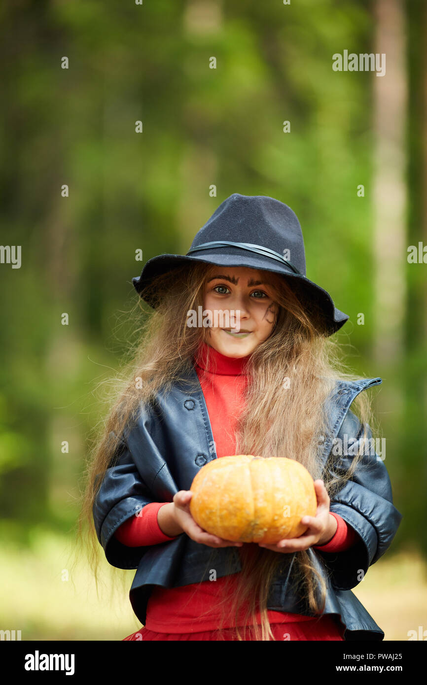 Kleines Mädchen in schwarzen Jacke und Hut Holding reif Halloween Kürbis, während Sie sie Stockfoto