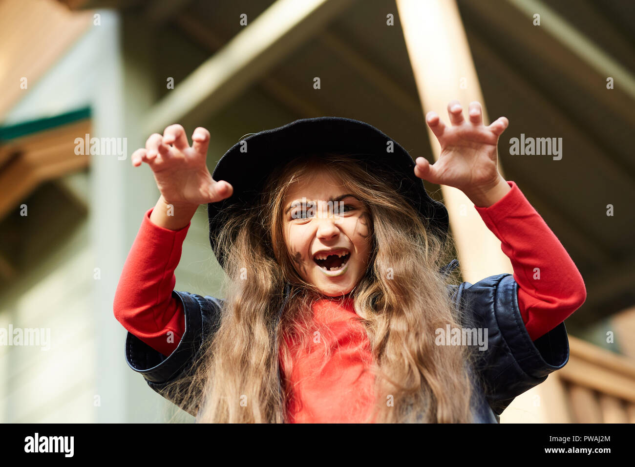 Unheimlich kleine Hexe in schwarzen Hut und Jacke und roten Pullover biegen ihre Finger, während sie erschreckend Gesichtsausdruck Stockfoto