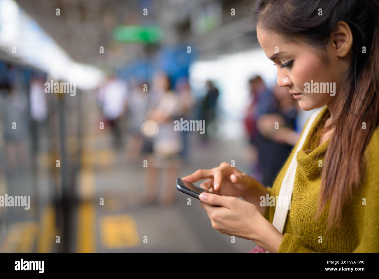 Junge schöne asiatische Frau mit Handy am Bahnhof Stockfoto