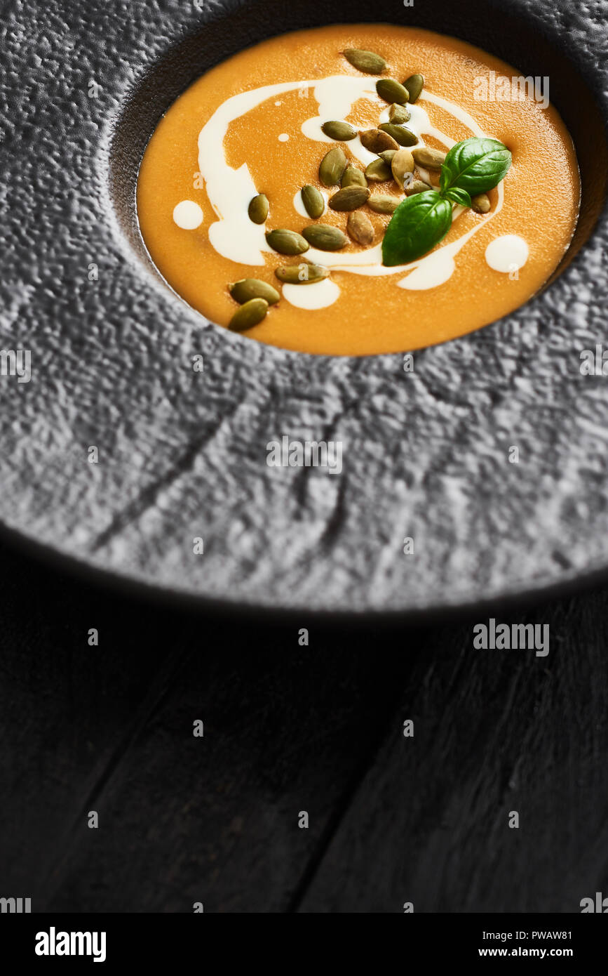 Nahaufnahme von Kürbis und Karotten Suppe mit Kürbiskernen, Sahne und Basilikum in Schwarz moderne Platte auf dunklen Holztisch mit kopieren. Ansicht von oben. Stockfoto
