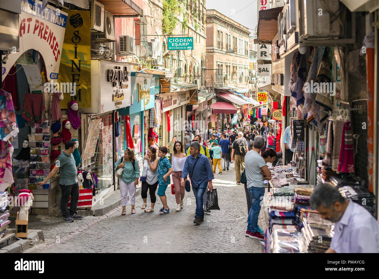 Reihen von Läden mit Waren auf Zeile einer hügeligen Straße mit Kopfsteinpflaster mit Menschen und Touristen spazieren im Stadtteil Fatih, Istanbul, Türkei Stockfoto