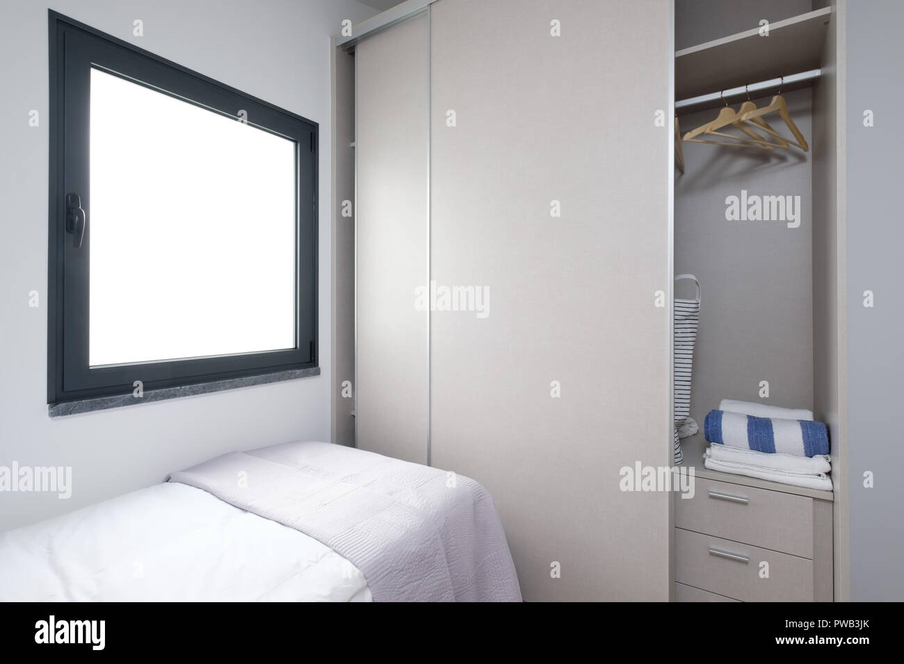 Kleines Schlafzimmer mit einem Bett, einem Kleiderschrank mit Schiebetüren und ein großes rechteckiges Fenster Stockfoto