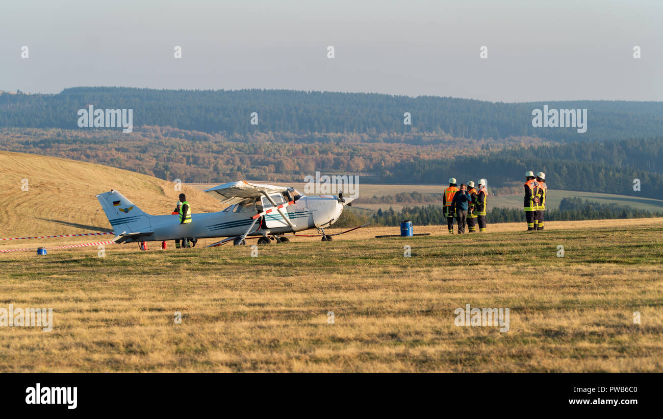 Gersfeld, Hessen. 14 Okt, 2018. 14. Oktober 2018, Deutschland, Gersfeld: Feuerwehrmänner stehen neben einem Sportflugzeug nach einem Flugzeugunglück. Das kleine Flugzeug war durch eine Schranke des Flugplatzes während einer gescheiterten Landung auf dem höchsten Berg hessens am Nachmittag gebrochen und verfing sich Passanten auf einem Bürgersteig. Zwei Frauen und ein Kind bei dem Unglueck ums Leben, fünf weitere wurden verletzt. Credit: Joscha Reinheimer/Joscha Reinheimer/dpa/Alamy leben Nachrichten Stockfoto