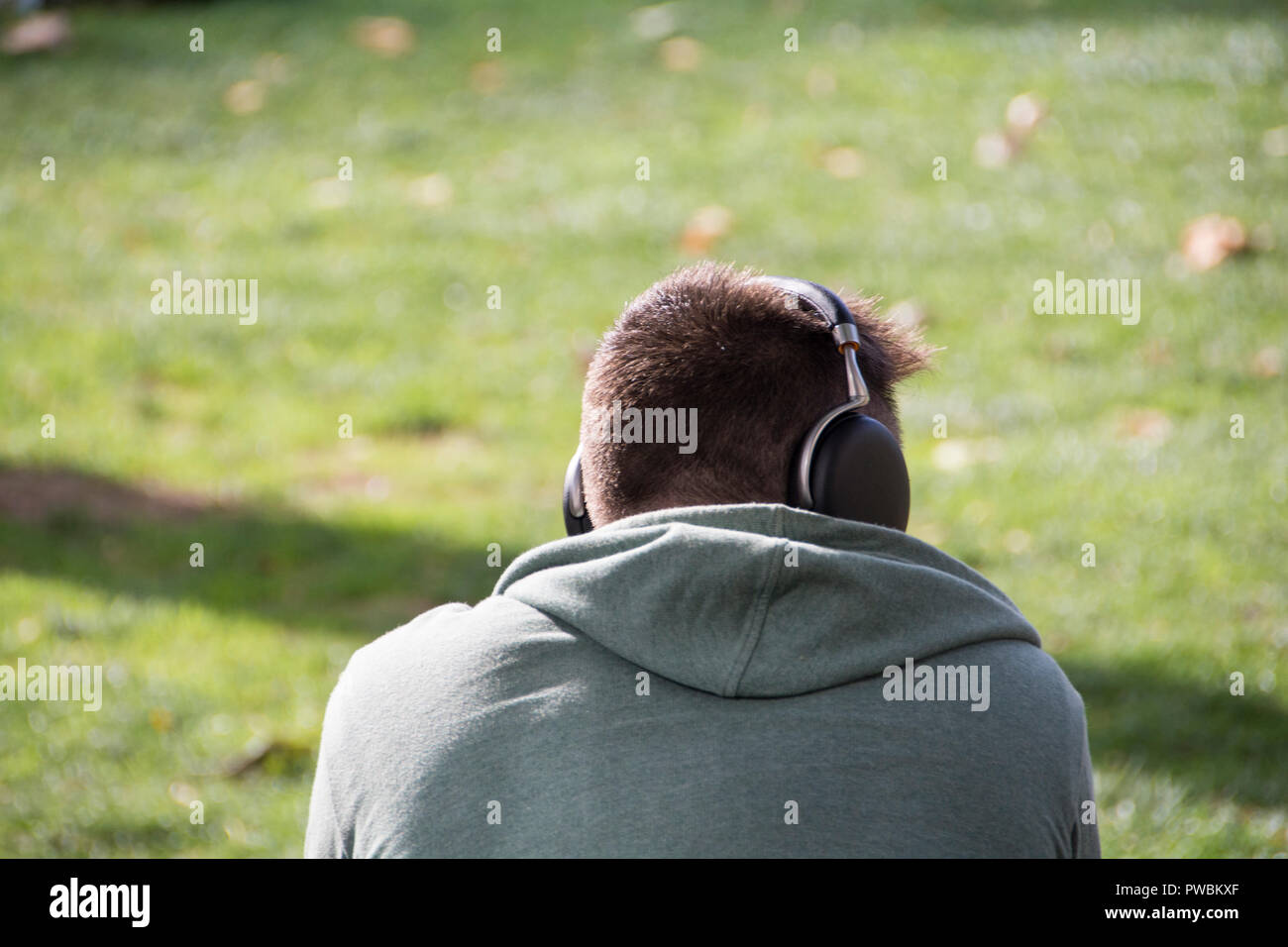Ein einsamer junger Mann mit Kopfhörern alleine auf einer Parkbank sitzt in London, Großbritannien Stockfoto