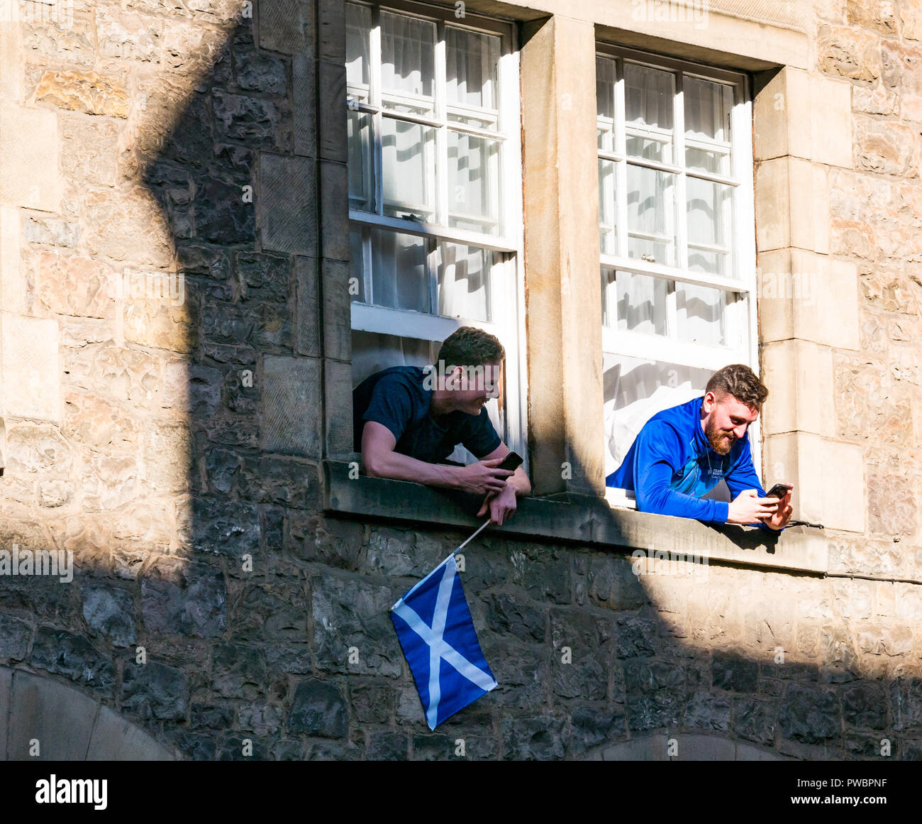 Junge Männer lehnte sich aus dem Fenster beobachten die schottische Unabhängigkeit Alle unter einem Banner AUOB März, Royal Mile, Edinburgh, Schottland, Großbritannien Stockfoto