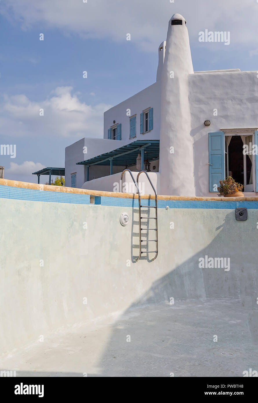 Leeren Swimmingpool. Ein typisch kykladischen Architektur einer griechischen Insel Haus im Hintergrund. Stockfoto