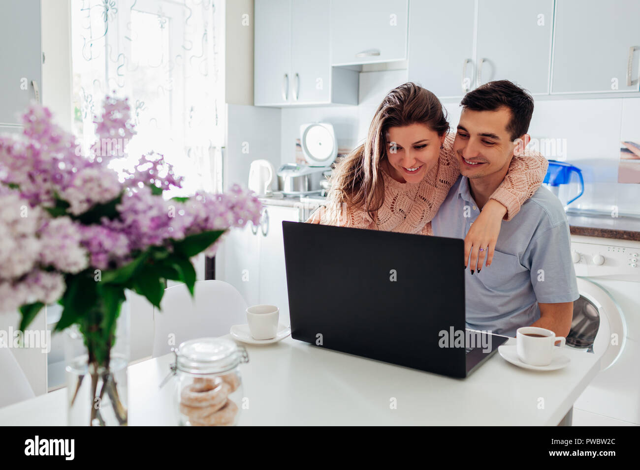 Glückliche Familie Paar mit Laptop beim Frühstück in der modernen Küche. Junger Mann und Frau prüfen Social Network News Stockfoto