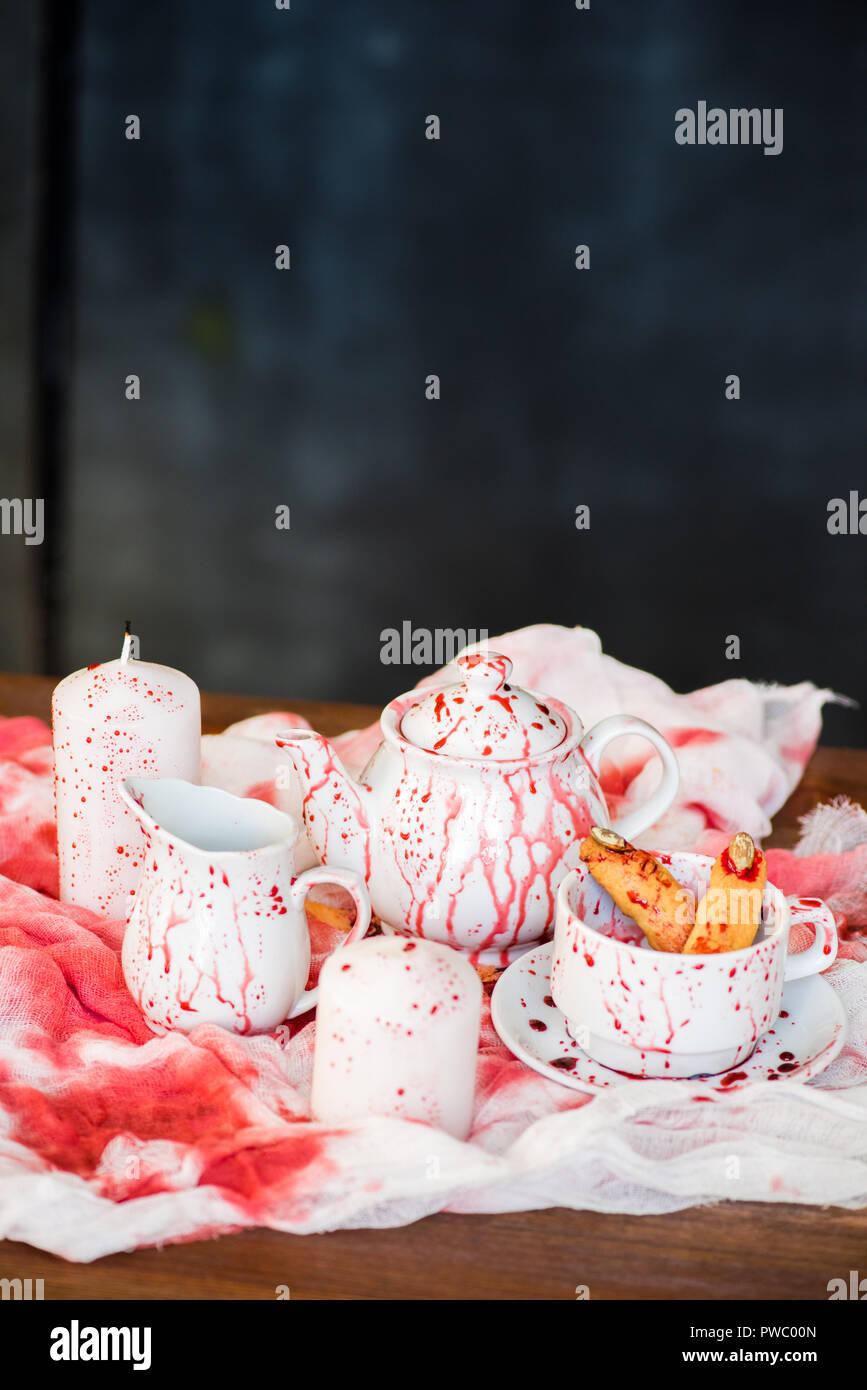 Kaffee Geschirr im Blut: Close-up von Keramik Teekanne, Milch Krug, Tasse Hexe Finger Cookies in blutigen Fleck auf schmutzige Fabric Stockfoto