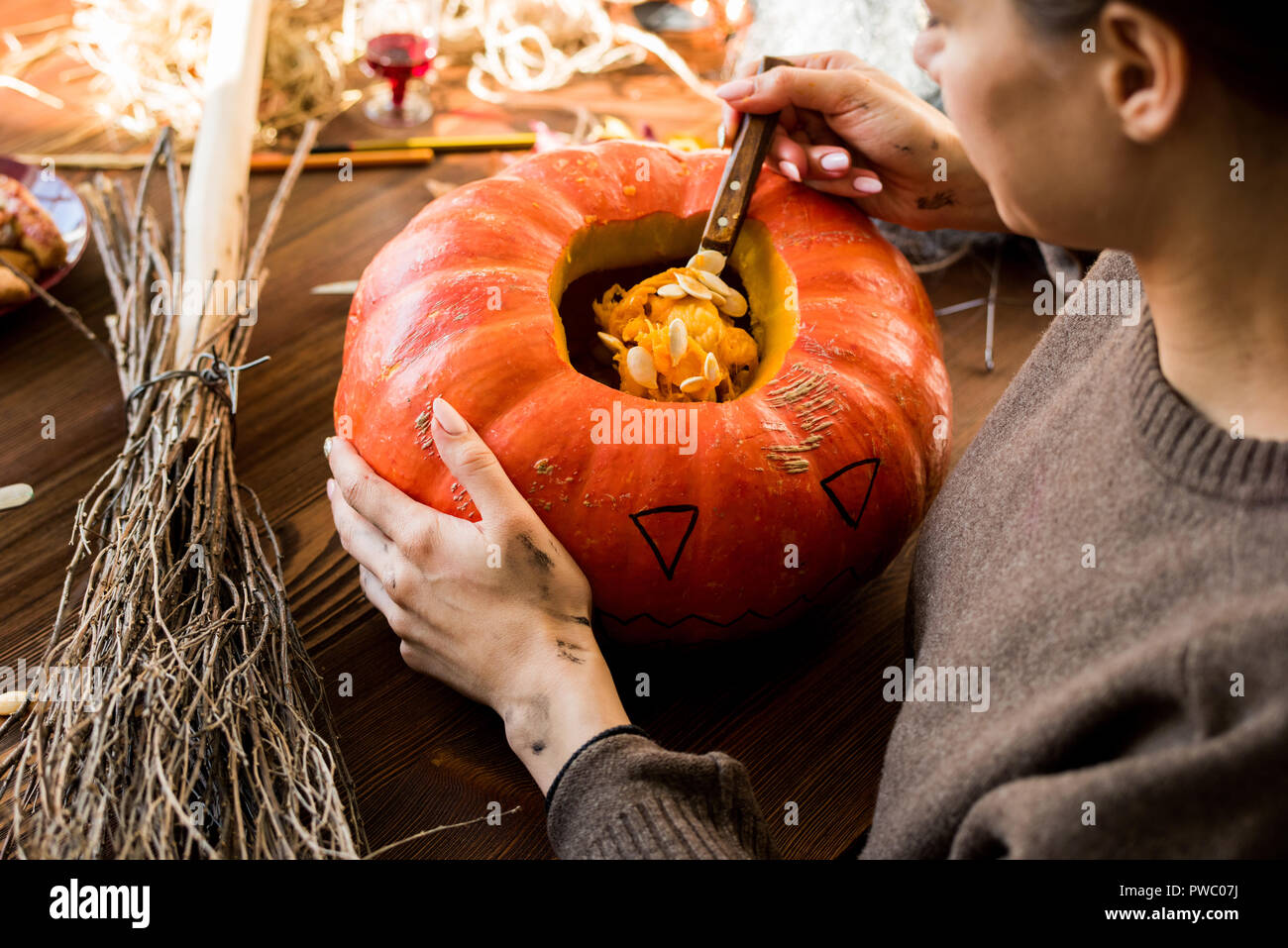 Close-up von konzentriertem Frau in Pullover sitzen am Tisch mit Besen und Schaufeln, Kürbiskerne, während sie Jack-o-Lantern in Werkstatt Stockfoto